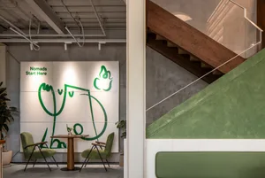Industrial restaurant interior with green walls, wooden stairs, and dining tables with chairs, a potted plant adding greenery to the space