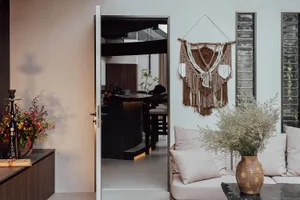 Open living area with white walls and floors, featuring two couches, a chair, potted plants, and vases, with a clean and bright atmosphere