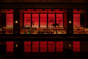A bar area with a long wooden counter featuring numerous bottles of liquor and a wine glass, set in a lively social atmosphere