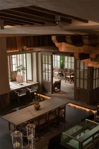 Warm and inviting restaurant interior with wooden floors and walls, featuring comfortable seating areas with chairs and potted plants