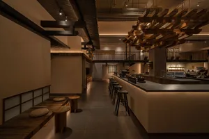 Modern restaurant interior with a bar and dining area featuring a bar, stools, chairs, and a dining table, with warm lighting creating a welcoming atmosphere