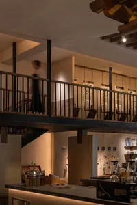 A calm and inviting interior space with a wooden staircase, stone elements, and soft diffused lighting, featuring visitors exploring the exhibits