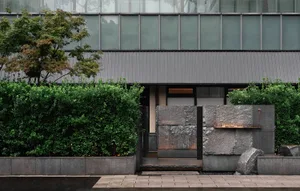 Modern building with a large stone wall and doorway, set against a natural backdrop of trees