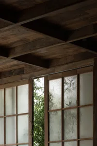 Warm and inviting room with wooden walls, ceiling beams, and a bamboo plant growing through a window