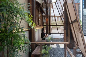 A calm and relaxed indoor space with a wooden bench in front of a window, surrounded by people socializing and enjoying the view