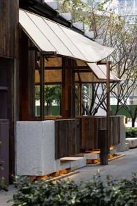 An open-air restaurant with wooden walls and a thatched roof, featuring two wooden benches and a relaxed atmosphere