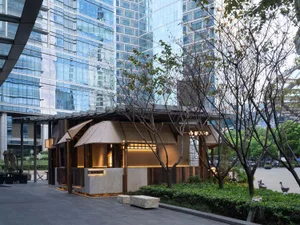 Cozy outdoor cafe with a wooden shelter, dining table, and chairs, situated in front of a tall building with a motorcycle parked nearby
