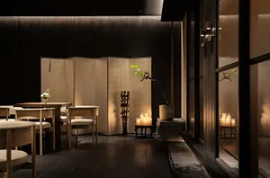 A warm and inviting Asian restaurant interior with wooden tables and chairs, a potted plant, and comfortable seating for guests