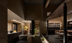 A warm and inviting restaurant dining area with a dining table, chairs, potted plants, and a kitchen in the background