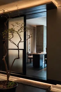 Dining room with a modern feel, featuring a dining table and chairs, a potted plant, and a large window providing natural light