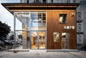 木質外觀的現代烘焙店門面，搭配玻璃門及室內桌椅，為顧客營造溫馨的氛圍