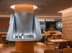 現代風格休閒餐廳用餐區，設有桌椅，並展示大型銀色碗，周圍有人坐著或站立