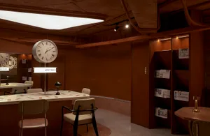 A modern showroom with a large clock on display, two chairs, and a table, set in a well-lit space with a bright atmosphere