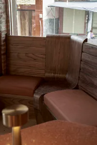 A cozy room with a wooden bench and brown leather seat, natural light from a window, and two people present