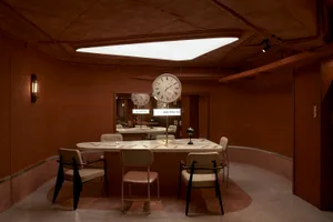 A modern restaurant interior with a circular dining table surrounded by chairs, featuring two clocks and a cozy atmosphere