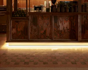 Cozy restaurant interior with wooden floors and walls, featuring a counter, sink, and refrigerator, with potted plants and various cups and bottles