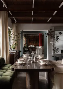 Warm and inviting dining space with a wooden table, chairs, and potted plants, set with various items and decorative vases