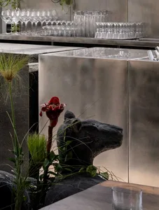 A modern interior design featuring a metal sculpture of a dog on a stone pedestal with a red flower and wine glasses, creating a sophisticated and inviting atmosphere