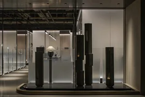 Elegant showroom with a glass wall displaying various sculptures and vases, featuring stone and organic shapes, in a sophisticated atmosphere