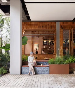 A casual indoor space with a wooden floor, potted plants, and people seated on benches and standing nearby
