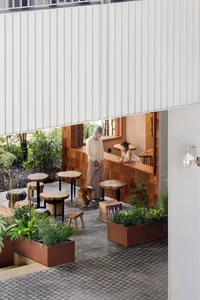 Casual outdoor cafe with wooden tables and chairs, surrounded by potted plants and situated in a wooded area