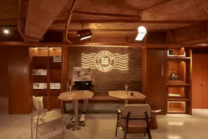 A warm and inviting cafe with brick walls, wooden furniture, and a cozy atmosphere, featuring a dining area with tables and chairs, and a person sitting at one of the tables