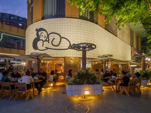 An outdoor dining area at night with tables, chairs, and umbrellas, featuring people socializing and enjoying their time together