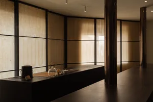 Cozy modern dining space with a wooden table, chairs, cups, a bowl, and a vase, dimly lit