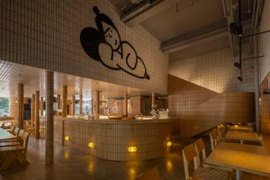 A restaurant interior with a counter and stairs, featuring a unique black and white mural on the walls, and comfortable seating areas with chairs