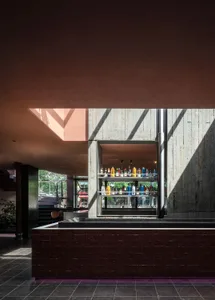 A modern bar area with red brick walls, concrete elements, and bottles on a shelf behind the counter, creating a warm and welcoming atmosphere