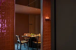 Dimly lit dining area with a wooden table, chairs, and cups, creating a warm and inviting atmosphere