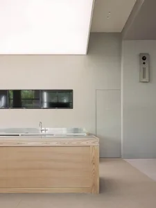 Empty kitchen with a wooden finish, a sink, and a large flat screen TV mounted on the wall, with two remotes nearby