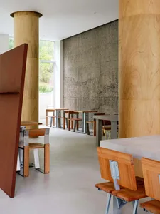A modern restaurant interior with wooden panel walls, multiple tables, chairs, and benches, creating a warm and inviting atmosphere