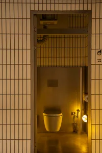 A functional bathroom with two metal sinks, a white toilet, and a mirror above one of the sinks, set against a yellowish background