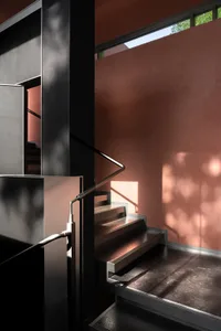 A photo of a modern staircase with a metal railing, pink walls, and a window allowing natural light to enter the space