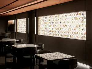 Dimly lit restaurant with multiple tables and chairs, glass walls, and natural light from a large window