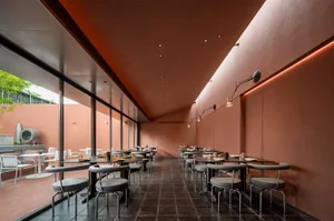 Modern restaurant interior with a dining area featuring tables, chairs, and potted plants, with reddish walls and a warm ambiance