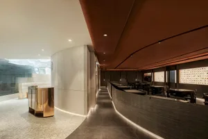 A modern restaurant interior with a long counter, dining tables, and a contemporary atmosphere, featuring wood and metal materials