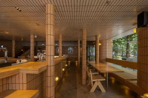 A modern restaurant interior with wooden walls and floors, featuring dining tables, chairs, and lighting fixtures