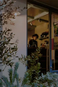 A cozy wine shop with a woman behind the counter, surrounded by bottles and chairs, creating a warm and inviting atmosphere