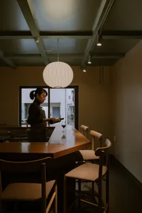 A woman stands near a wooden dining table surrounded by chairs in a relaxed and inviting restaurant atmosphere