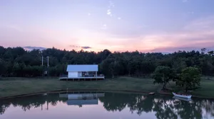 A serene wooden house on a hillside overlooking a lake, with a large deck and two chairs