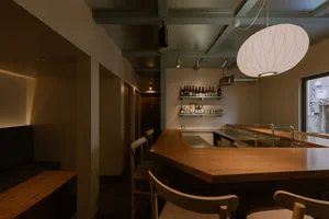 Cozy kitchen with wooden floors and walls, featuring a dining area with chairs and wine glasses, and a countertop with bottles