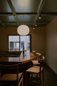 A cozy bar area with wooden chairs and a dining table, a bottle of wine, and a sink in the background