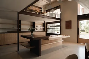 Open living area with wooden floors and walls, featuring a dining table, chairs, potted plant, and vases, with a warm and inviting atmosphere