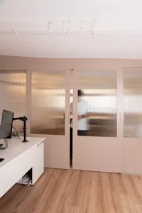 Office space with a wooden floor, natural light, and a man standing inside one of the rooms