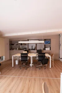 A modern office space with a large white table surrounded by multiple chairs on a wooden floor, creating a warm and inviting atmosphere