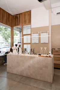 A cozy coffee shop interior with a marble counter, cups, bottles, and bowls on display, and two people standing near the counter