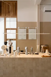 A cozy coffee shop interior with a counter, whiteboards, and various coffee machines and cups on display, surrounded by exposed brick walls and comfortable seating