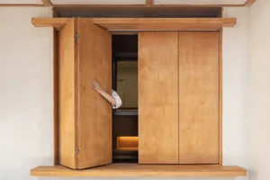 A person stands in an open doorway of a rustic wooden cabin, peeking through with a sense of curiosity and anticipation